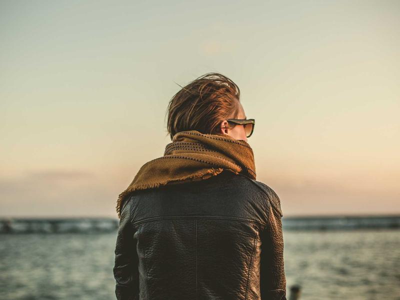 Person in a leather jacket and scarf gazing out at the sea during sunset