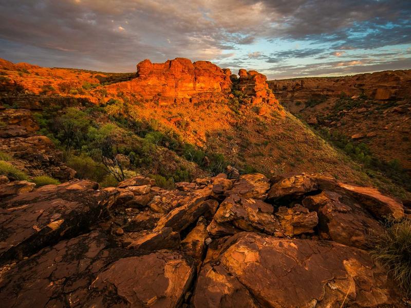 Red sandstone canyon formations glowing at golden hour under a cloudy sky