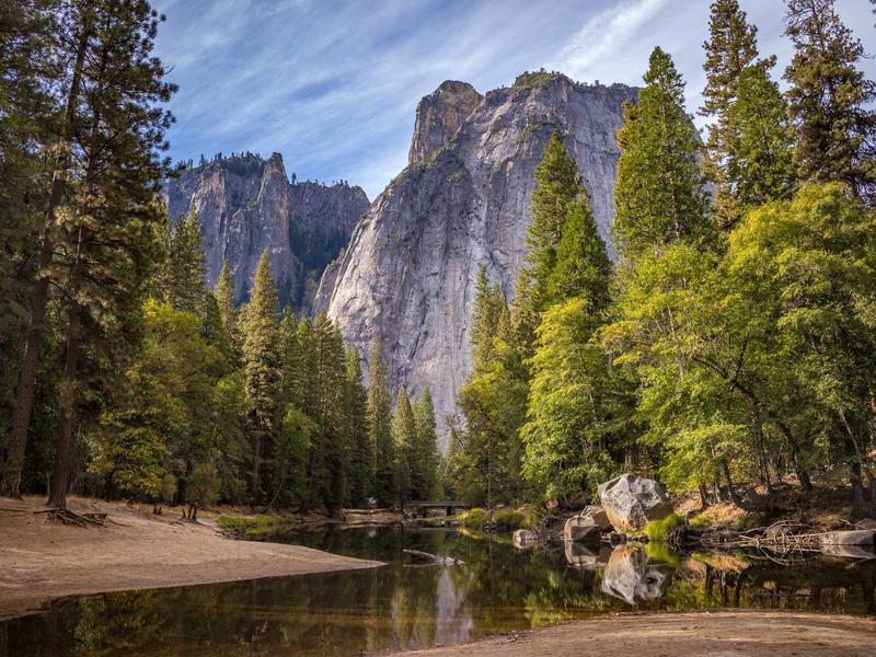 Calm river reflecting towering granite cliffs framed by pine trees